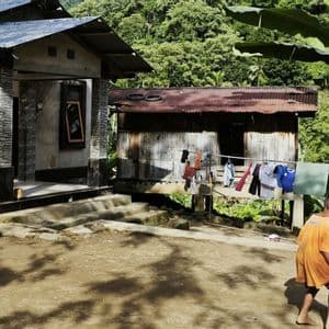 In einem ländlichen Dorf spielen zwei barfüßige Jungen auf einem staubigen Hof Fußball, während andere auf einer Veranda sitzen.