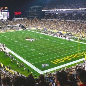 Una vista panoramica di uno stadio di football americano affollato durante una partita notturna, con 'Pittsburgh' dipinto nella endzone del campo.
