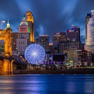 Ponte illuminato e ruota panoramica sul lungofiume con skyline cittadino di notte.