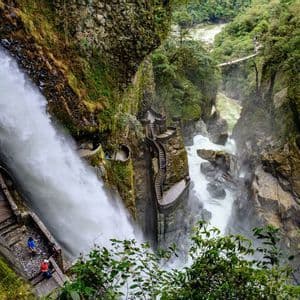 Un groupe de personnes d'un voyage WeRoad sur un escalier en pierre raide et sinueux à côté d'une grande cascade dans une gorge rocheuse et verte.