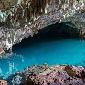 Une grande caverne souterraine abritant un bassin d'eau turquoise limpide, avec de nombreuses stalactites pendant du plafond.