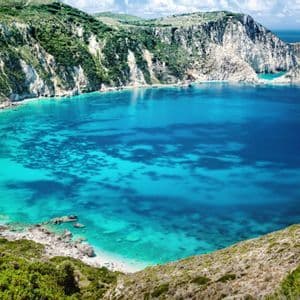 Una vista dall'alto di una cala appartata con acqua turchese, una spiaggia sabbiosa con persone e ripide scogliere verdi e bianche.