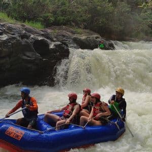 Eine WeRoad Gruppenreise Wildwasser-Rafting in einem blauen Schlauchboot auf einem Fluss mit Stromschnellen und einem Wasserfall.