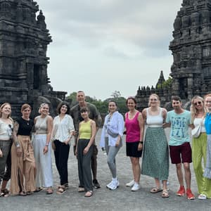 Eine WeRoad-Gruppenreise posiert für ein Foto vor zwei großen, verzierten Steintempeln unter einem bewölkten Himmel.