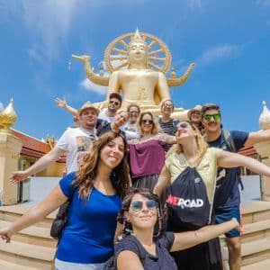 Un viaje en grupo de WeRoad posando para una foto en las escaleras de un templo frente a una gran estatua dorada de Buda bajo un cielo azul.