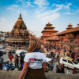 De dos, un chef de groupe WeRoad contemple une place de ville animée remplie de temples historiques, de gens et de véhicules.