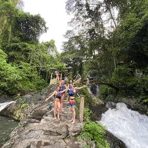 Eine WeRoad-Gruppenreise posiert mit offenen Armen auf Felsen neben einem rauschenden Wasserfall in einem dichten Dschungel.