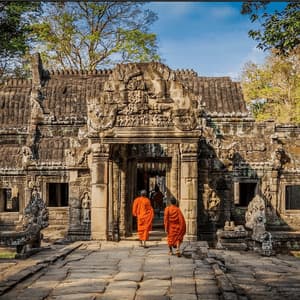 Zwei Mönche in orangefarbenen Roben gehen auf einem Steinpfad auf den verzierten Eingang eines alten Tempels zu.