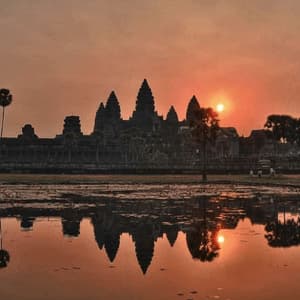 Die Silhouette eines großen alten Tempels bei Sonnenaufgang, wobei sich seine Türme und Form in einem stillen Teich im Vordergrund spiegeln.