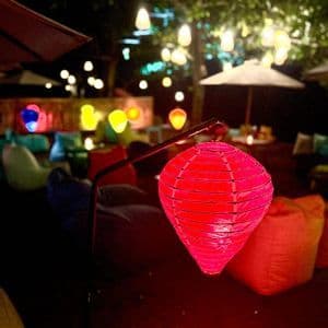 Nachts erhellt eine rosa Papierlaterne eine Außenlounge, die mit bunten Sitzsäcken und Hängelampen gefüllt ist.