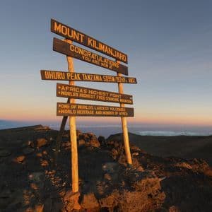 The summit sign at Uhuru Peak on Mount Kilimanjaro, standing on rocky ground at sunrise.