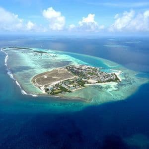 Una vista aérea de una isla poblada rodeada por una laguna turquesa, arrecifes de coral y el vasto océano azul profundo.