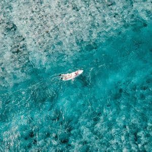 Vista aérea de una persona en una tabla de surf remando en agua clara y turquesa.