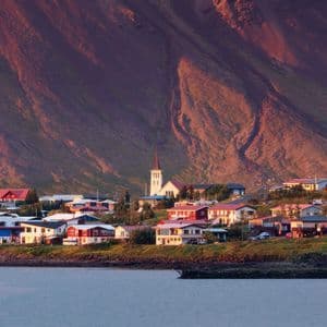 Ein Küstendorf mit einer Kirche und bunten Häusern am Fuße eines großen Berges bei Sonnenuntergang.