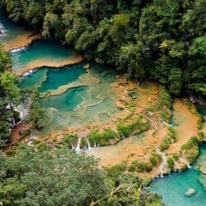 Eine Luftaufnahme von gestuften türkisfarbenen Wasserbecken und Wasserfällen, die durch einen dichten grünen Wald fließen.