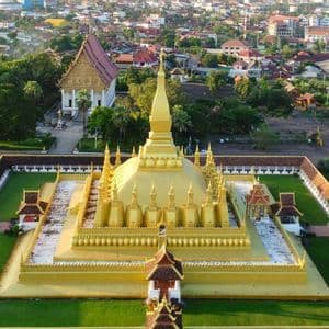Eine Luftaufnahme einer großen, goldenen Stupa mit mehreren Türmen, umschlossen von einem ummauerten Hof, mit einer Stadt im Hintergrund.