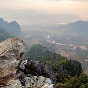 Ein Blick von einem felsigen Gipfel über ein diesiges Tal mit grünen Kalksteinkarsten und einem Heißluftballon in der Ferne.