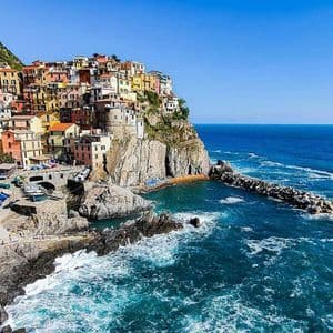 Casas de colores construidas en un acantilado escarpado y rocoso, con vistas a un mar azul vibrante en un día soleado.
