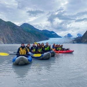 Eine WeRoad Gruppenreise beim Kajakfahren auf einem ruhigen See, mit einem großen Gletscher und Bergen in der Ferne.