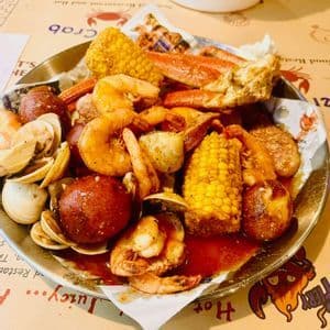 A close-up of a metal tray with a seafood boil of shrimp, crab legs, clams, corn, and potatoes covered in a red sauce.