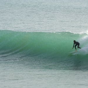 A surfer in a black wetsuit rides along the face of a large, green wave in the open ocean.