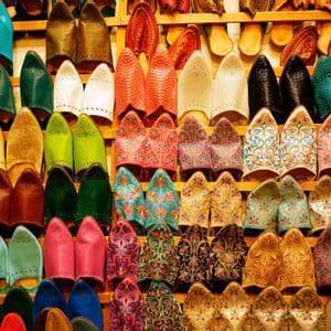 Dozens of colorful traditional leather slippers with pointed toes arranged on wooden display shelves.