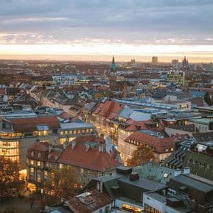 Una vista aérea de un paisaje urbano con muchos edificios, algunos iluminados, bajo un cielo nublado al anochecer.
