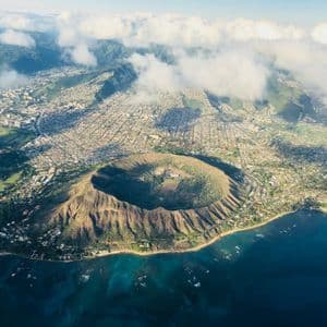 Vista aerea di un grande cratere vulcanico circolare su una costa accanto a una città popolosa e acque blu dell'oceano.
