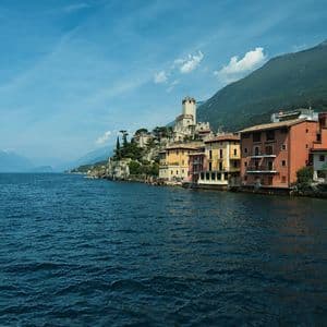 A lakeside village with colorful houses and a castle on a cliff, seen from the water with a mountain behind.