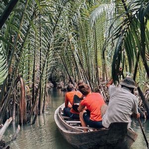 A WeRoad group trip travels by wooden boat through a narrow canal lined with dense, tall palm trees.