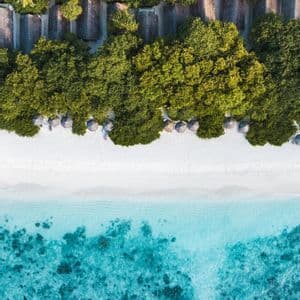 Una vista aerea di un resort tropicale dove la foresta lussureggiante incontra una spiaggia di sabbia bianca e l'oceano turchese.