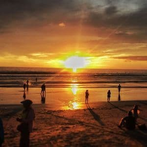 Menschensilhouetten am Strand beobachten einen lebhaften orangefarbenen Sonnenuntergang über dem Meer.