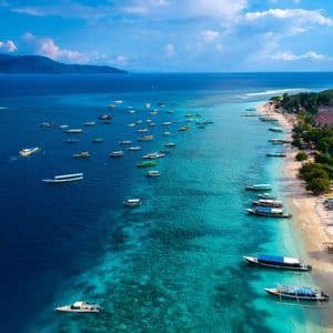 Luftaufnahme vieler Boote in klarem, türkisfarbenem Wasser an einem Sandstrand mit Gebäuden und Bäumen.