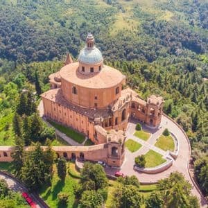 Una veduta aerea di un grande santuario a cupola su una collina, circondato da una lussureggiante foresta verde e un portico ad arco.