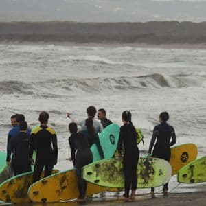 Un viaggio di gruppo WeRoad con persone in muta e tavole da surf su una spiaggia, mentre osservano le onde agitate.