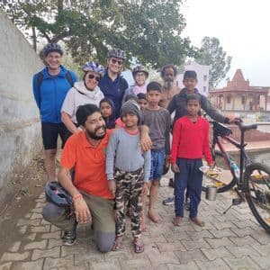 Un gruppo di ciclisti WeRoad in posa con bambini e adulti del luogo su un sentiero lastricato, con un tempio sullo sfondo.