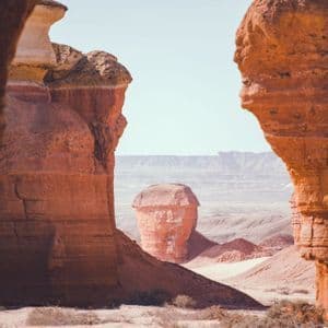 Una singolare formazione rocciosa rossa in un paesaggio desertico, ammirata attraverso una fessura nelle scogliere di arenaria.
