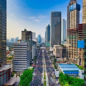 Vista cenital de una gran multitud llenando una calle ancha entre rascacielos modernos bajo un cielo azul.