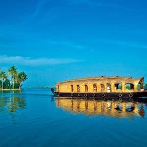 Ein traditionelles Holzhausboot mit Reetdach schwimmt auf ruhigem blauem Wasser, mit Palmen an einem fernen Ufer.