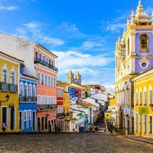 Des bâtiments coloniaux colorés et une église historique bordent une rue pavée sous un ciel bleu éclatant parsemé de nuages légers.