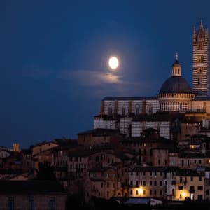 Una cattedrale e un campanile illuminati si ergono su una città storica sotto la luna piena di notte.