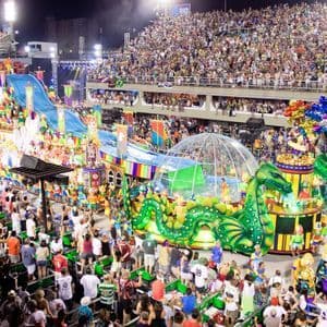 Un char de défilé immense et coloré avec un dragon vert traverse un stade rempli de spectateurs la nuit pendant un carnaval.