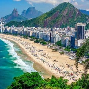 Vue plongeante d'une plage de sable bondée, longeant une ville tentaculaire au pied de montagnes verdoyantes.