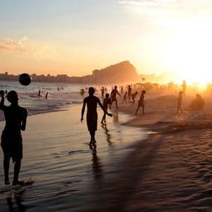 Silhouettes de personnes jouant au ballon sur une plage bondée au coucher du soleil sur l'océan et une ville lointaine