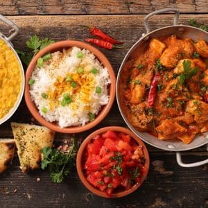 Eine Vogelperspektive auf indische Gerichte, darunter Hühnercurry, Dal, Reis, Salat und Brot, angerichtet auf einem dunklen Holztisch.