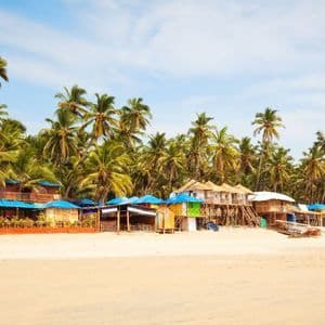 Bunte Strandhütten und Bungalows an einem Sandstrand vor einem Palmenwald.