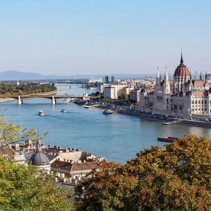 Vue surélevée d'un grand bâtiment gouvernemental orné, sur les rives d'une large rivière, avec des bateaux et un pont sous un ciel clair.