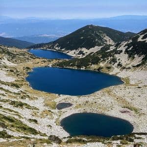 Escursionisti di un viaggio di gruppo WeRoad su un sentiero roccioso che domina diversi laghi alpini di un blu profondo in una valle di montagna.