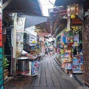 Menschen gehen eine schmale, holzbeplankte Gasse entlang, die von farbenfrohen Marktständen und Geschäften gesäumt ist.