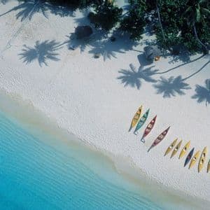 Una vista aerea di kayak colorati allineati su una spiaggia di sabbia bianca accanto all'acqua turchese, con le ombre delle palme.